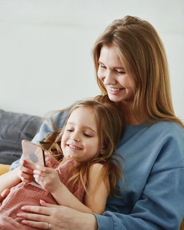 Madre e hija sonriendo juntas en el sofá de su casa, mirando un celular